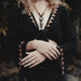 Person wearing a black top with geometric patterns and a necklace, standing in a natural setting.