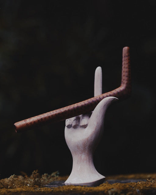 White ceramic hand holding a brown rod against a dark background