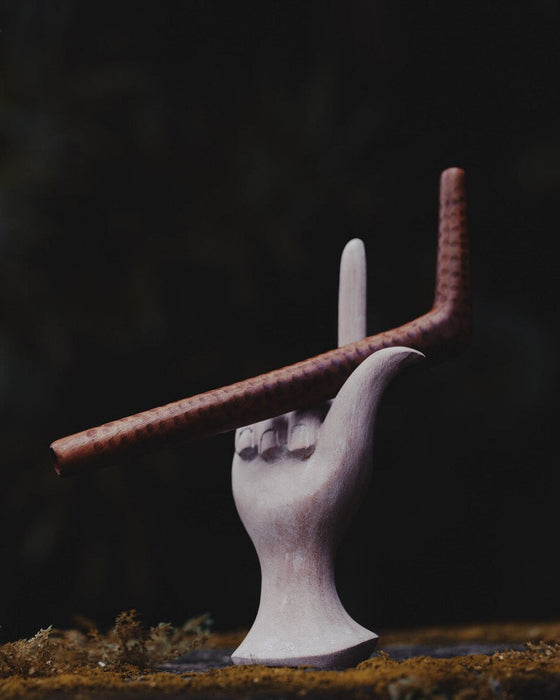 White ceramic hand holding a brown rod against a dark background