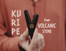 Hand holding a black tool with 'Kuripe' and 'from Volcanic Stone' text on a red background