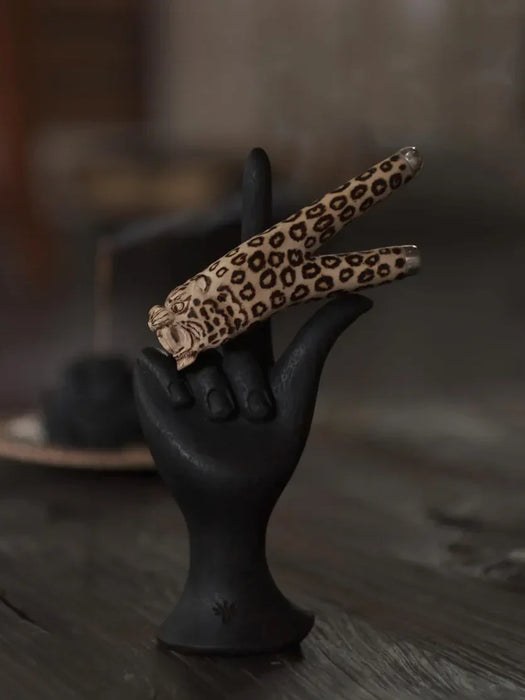 Leopard print hair clips on a black hand-shaped stand with a blurred background