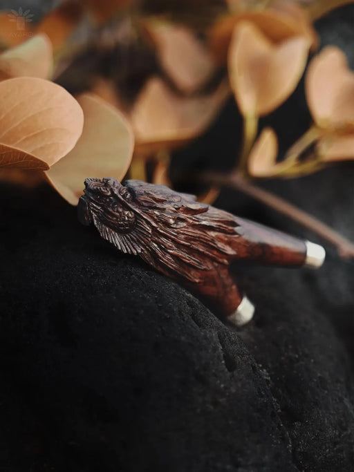 Wooden angel wing figurine on a dark surface with blurred leaves in the background