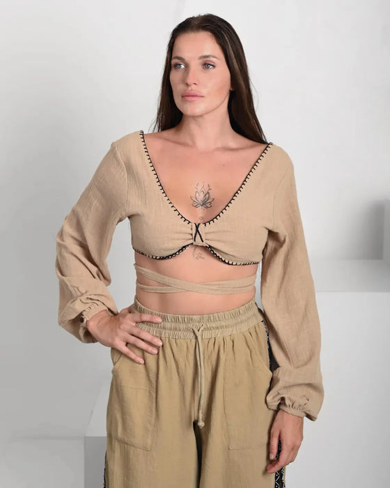Woman wearing a beige outfit with long sleeves and a crop top against a white background