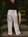 Person wearing white pants with tribal designs and a belt, holding a gong outdoors.