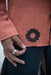 Person wearing a red garment with a black geometric design, holding their hand to their waist.