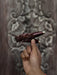 Hand holding a decorative wooden object against an ornate wooden background
