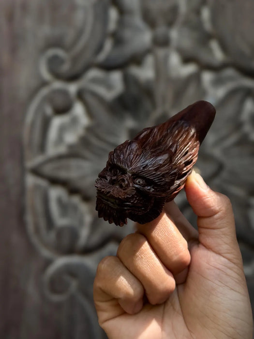 Hand holding a dark brown wooden figurine against a decorative metal background