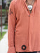 Person wearing a peach-colored shirt with black patterns, standing outdoors.