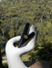 Black jewelry box held by a white hand sculpture against a blurred green forest background