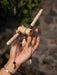 Hand holding a decorative item made of sticks and beads against a blurred natural background