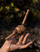 Hand holding a wooden tool with a textured handle against a natural background