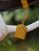 Gold pendant hanging from a branch with a blurred natural background