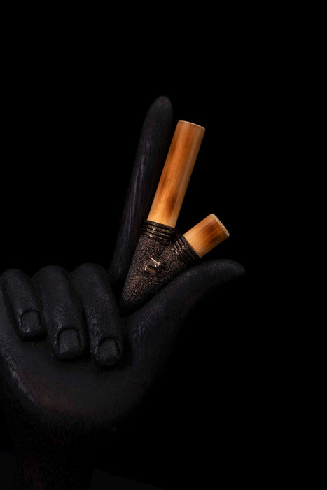 Two makeup brushes with wooden handles held by a dark-skinned hand against a black background