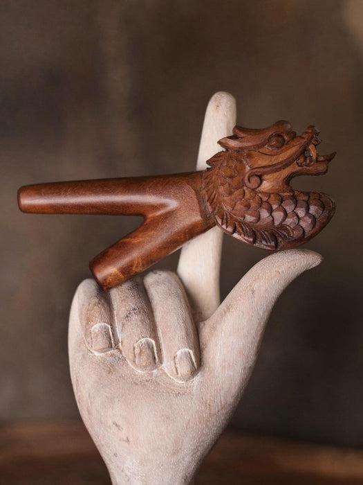 Wooden dragon figurine on a stone hand against a brown background