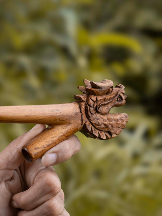 Wooden tool with intricate carvings held by a hand against a blurred natural background