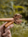 Wooden tool with intricate carvings held by a hand against a blurred natural background