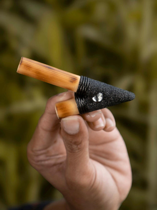 Hand holding a small gardening tool with a wooden handle and black pointed head against a blurred green background
