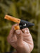 Hand holding a small gardening tool with a wooden handle and black pointed head against a blurred green background