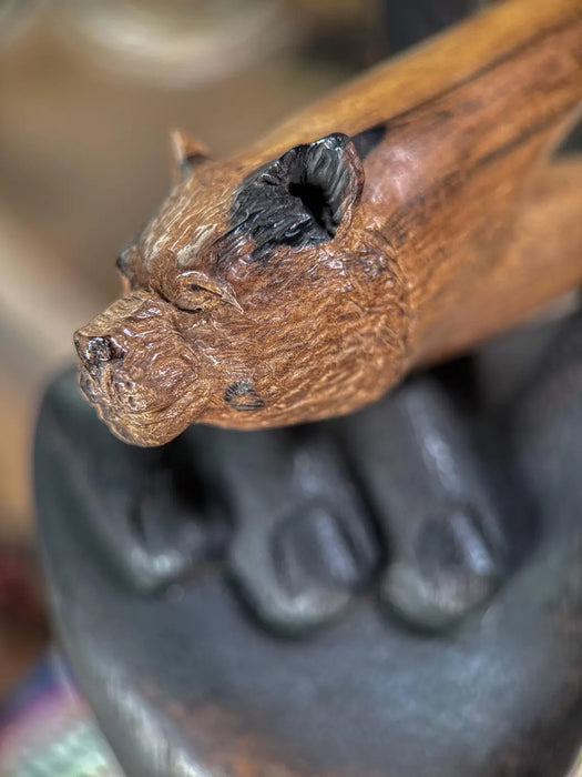 Close-up of a wooden object with a bear head design held by a person wearing black gloves.