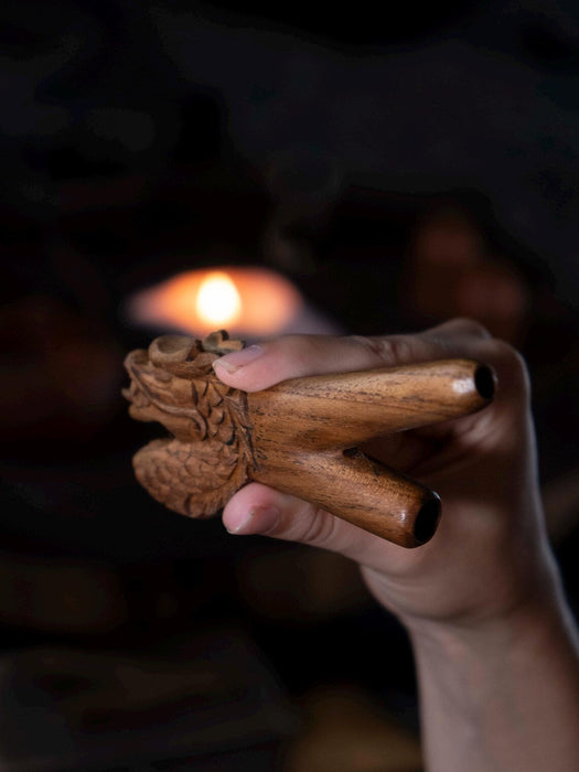 Hand holding a wooden incense burner with a blurred candle in the background