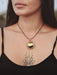 Woman wearing a black tank top with a gold pendant necklace, showing a tattoo on her chest.
