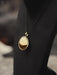 Gold pendant on a black cord against a blurred background