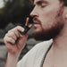 Man applying lipstick outdoors with a blurred background