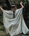 A person enveloped in a handmade Boho tribal cotton poncho, embracing the serenity of nature at a waterfall, reflecting a unisex shamanic clothing style