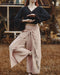 Person wearing a dark sweater and light pink pants with floral embroidery in an outdoor setting.